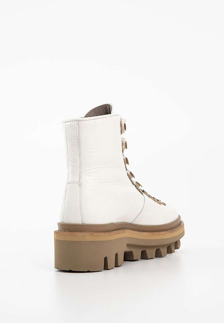 Weiße Lederstiefeletten mit einer klobigen braunen Sohle, runder Spitze und goldenen Ösen für die Schnürsenkel. Strukturiertes Finish und kontrastierende Sohlenhöhe.