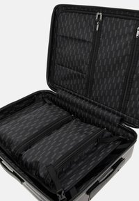 Valigia rigida nera con scomparti con zip, dotata di un rivestimento interno a motivo con il marchio ripetuto "GUESS". Manico testurizzato per una migliore presa.
