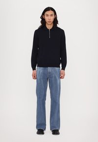 Tengerészkék kötött póló ing, cipzáras nyakkivágással, világoskék, kenguru szabású farmerral párosítva. Egyszerű dizájn és sima textúra, laza szabással.