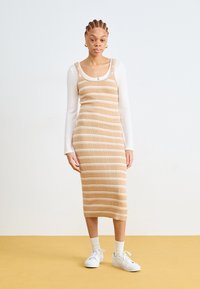 Strikket midikjole i beige med hvite horisontale striper, har tynne skulderstropper, en ribbet tekstur og en kroppsnær silhuett.
