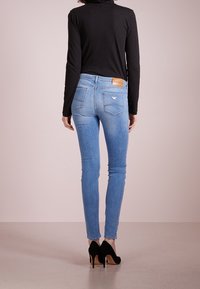 Smala blå jeans av denim, med en tan läder bakficka, bakfickor med V-söm, som bärs med svarta högklackade skor.