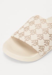 Sandal s trakama od bež tekstila s sjajnim, ponavljajućim uzorkom logotipa, uparen s mekanim, bijelim gumiranim potplatom.