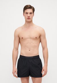 Pantaloni da bagno neri con vita elastica e logo Calvin Klein. Il tessuto sembra leggero e morbido, con una vestibilità rilassata.