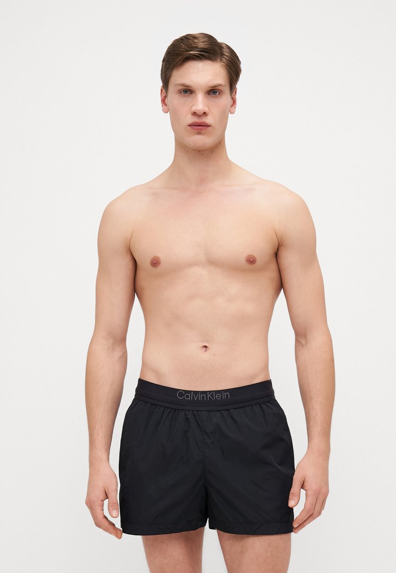 Pantaloni da bagno neri con vita elastica e logo Calvin Klein. Il tessuto sembra leggero e morbido, con una vestibilità rilassata.