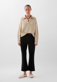 Beige knitted sweater with a collar, paired with high-waisted black flared jeans and light beige slip-on shoes with a ruffled edge.