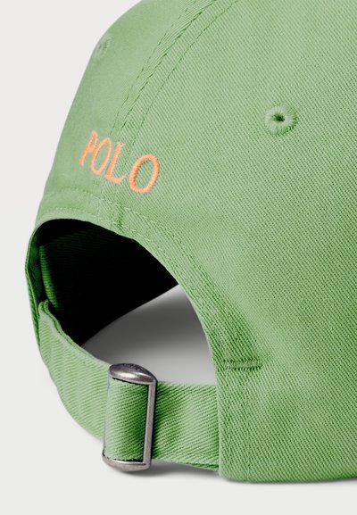 Căciulă din bumbac verde cu boruri curbate, având textul brodat "POLO" în portocaliu. Curea ajustabilă la spate cu elemente de metal, țesătură texturată.