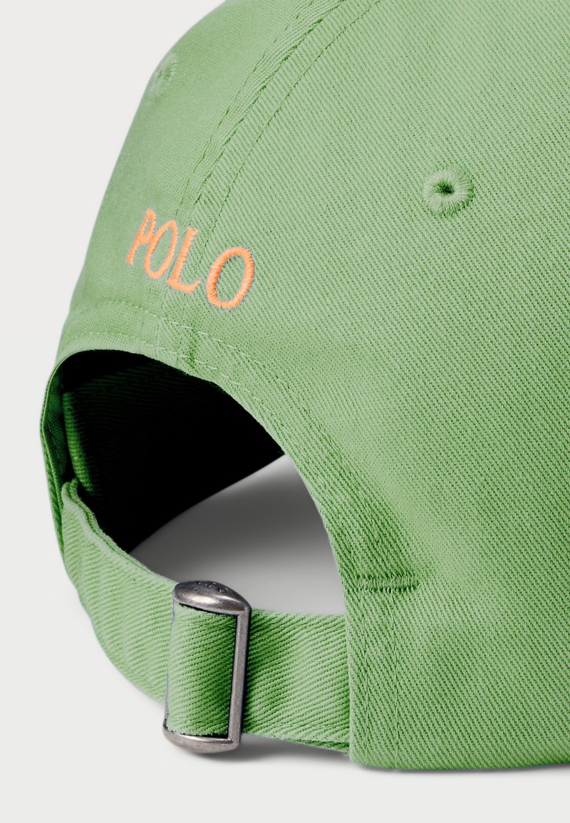 Grøn bomuldske med en buet skygge, prydet med orange broderet "POLO" tekst. Justerbar rem bagpå med metalhardware, tekstureret stof.