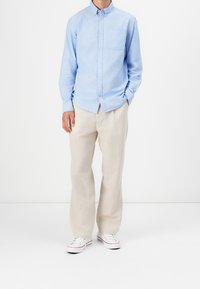 Camisa azul claro de botones con un bolsillo en el pecho, combinada con pantalones beige de corte holgado y zapatillas blancas con detalles rojos.