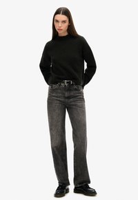 Pull en tricot noir avec un col rond, associé à un jean noir droit délavé et des chaussures à lacets noires. Design simple et épuré.