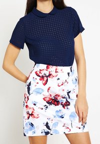 Marinblå kortärmad topp med ett strukturerat rutmönster och krage, kombinerad med en vit blommig kjol med röda och blå blommor.