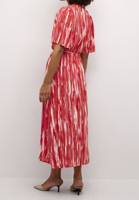 Robe longue à motif abstrait rouge et blanc. Elle présente des manches courtes froncées, une taille marquée, et un tissu fluide à texture lisse.