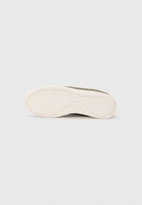 Semelle de chaussure de sport verte avec une semelle en caoutchouc blanc texturé, présentant des motifs circulaires et un léger talon. Design épuré sans marque visible.