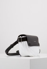 Borsa a tracolla in pelle nera con un frontale imbottito bianco, chiusura a scatto, tracolla regolabile e texture liscia. Presenta dettagli con il marchio.