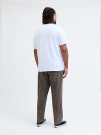 Vit bomullströja i kombination med löst sittande bruna kordflöjlsbyxor. Kläderna har en avslappnad design och en strukturerad textur.