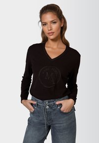 Schwarzer V-Ausschnitt-Pullover mit strukturiertem Logo, engen Ärmeln und gerippten Bündchen, kombiniert mit hellen Jeanshosen, die eine Kordelzug-Taille haben.