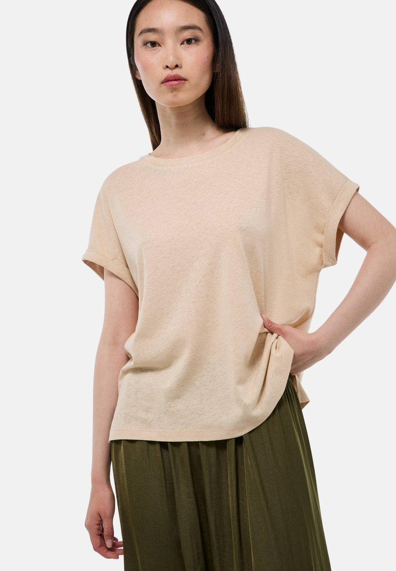 T-shirt beige à manches courtes avec une coupe décontractée, texture douce, col rond et manches roulées, associé à une jupe plissée verte.