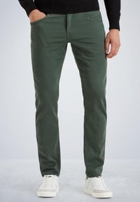 Pantalones de algodón verdes con un corte slim, diseño de cinco bolsillos y una textura suave; combinados con zapatillas blancas de caña baja.