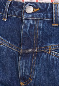 Mörkblå denimjeans med synlig sömnad, silverfärgad knäppning och en etikett på midjebandet. Avslappnad stil med klassiska designelement.