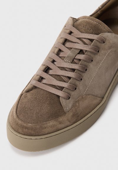 Brown suede sneaker with matching laces, beige rubber sole, and detailed stitching on a white background.