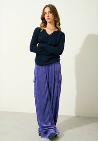 Granatowy sweter dzianinowy z dekoltem w serek i detalem guzika, zestawiony z luźnymi, prążkowanymi fioletowymi spodniami z korduroju z bocznymi kieszeniami.