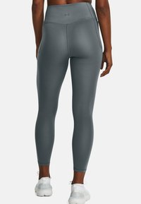 Leggings a vita alta, aderenti, in un materiale grigio uniforme con una texture liscia e dettagli di cucitura minimi, abbinati a scarpe da ginnastica bianche.