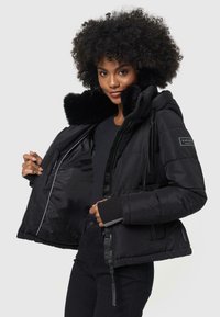 Manteau rembourré noir avec col en fausse fourrure, fermeture éclair à l'avant et cordon de serrage ajustable. Dispose de poches latérales et de poignets tricotés pour un confort supplémentaire.