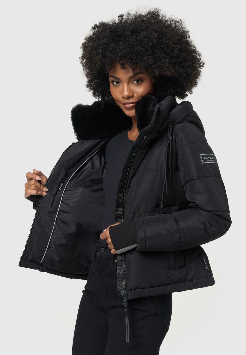 Manteau rembourré noir avec col en fausse fourrure, fermeture éclair à l'avant et cordon de serrage ajustable. Dispose de poches latérales et de poignets tricotés pour un confort supplémentaire.