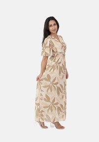 Vestido maxi en beige claro con estampados florales abstractos en oliva y coral. Mangas cortas, escote en V, cintura elástica, tejido fluido. Sandalias de tacón transparente.