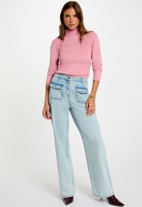 Maglione turtleneck a costine rosa chiaro abbinato a jeans a gamba larga, blu chiaro, a vita alta. Presenta due tasche posteriori e una chiusura con bottone.