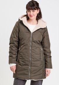 Parka matelassée vert olive avec une capuche en fausse fourrure beige. Dispose de poches à glissière et de longues manches avec des poignets en tricot. Texture lisse, design mi-mollet.
