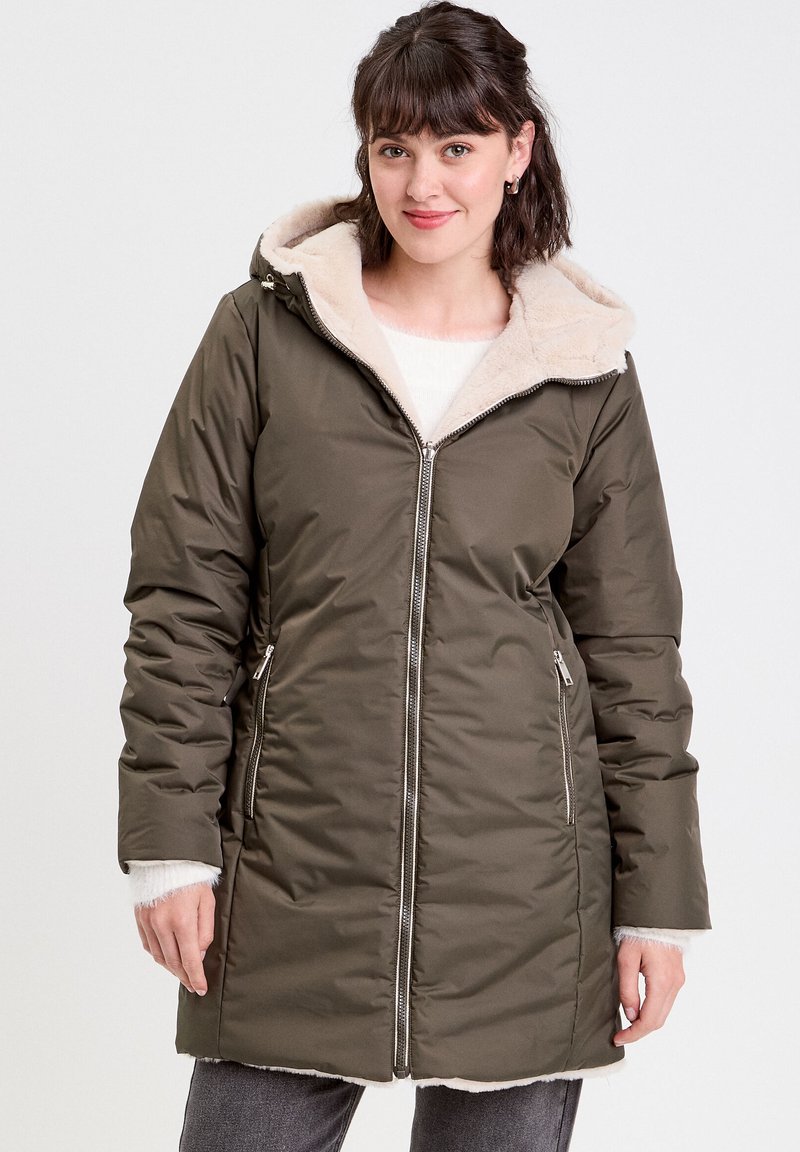 Parka matelassée vert olive avec une capuche en fausse fourrure beige. Dispose de poches à glissière et de longues manches avec des poignets en tricot. Texture lisse, design mi-mollet.