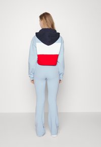 Ljusblå joggingdräkt med utsvängda ben, med en navy, vit och röd färgblockerad kortärmad hoodie. Mjuk fabrik med en slät textur.