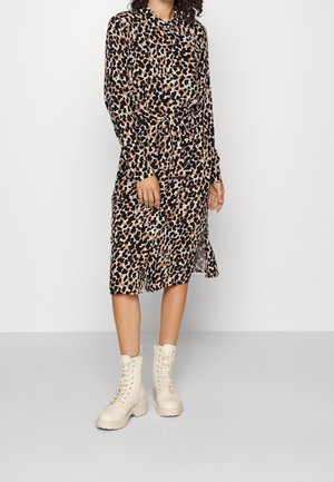 Mujer con un vestido de manga larga hasta la rodilla con estampado de leopardo y cinturón, combinado con botines crema con cordones.