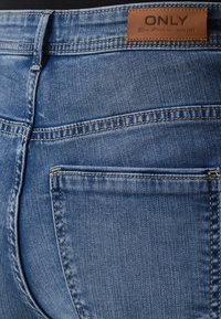Kék farmernadrág, textúrált felülettel, bőr címkével a deréknál, amelyen az "ONLY" felirat található, és kontrasztos varrással a zsebeknél.