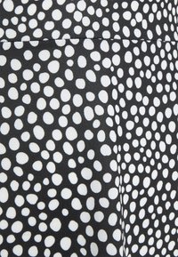 Tissu noir avec des pois blancs irréguliers et denses et une couture horizontale visible près du haut, créant un motif audacieux et texturé.