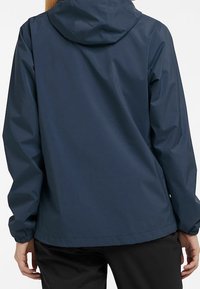 Veste de pluie bleu marine avec capuche, poignets élastiques et coupe droite. Texture lisse et design minimaliste, adaptée à la protection contre les intempéries.