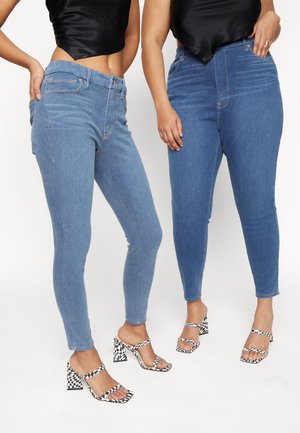 Two women wearing blue skinny jeans, black crop tops, and black-and-white checkered high-heeled sandals standing side by side.