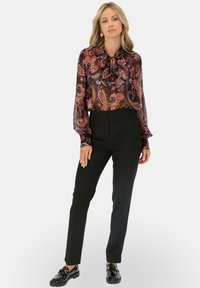 Czarne, wysokie spodnie połączone z przezroczystą, wzorzystą bluzką w paisley w odcieniach fioletu, pomarańczu i czerwieni.