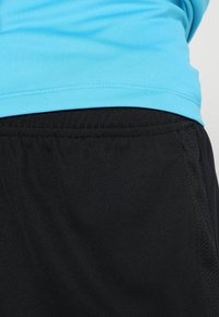Pantalones cortos atléticos negros con una textura suave, combinados con una camiseta ajustada de color azul claro hecha de un tejido transpirable. Detalles de costura visibles.