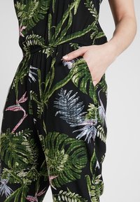 Mono negro con un vibrante estampado de hojas tropicales en verde y rosa. Cuenta con una cintura fruncida y bolsillos laterales para mayor funcionalidad.