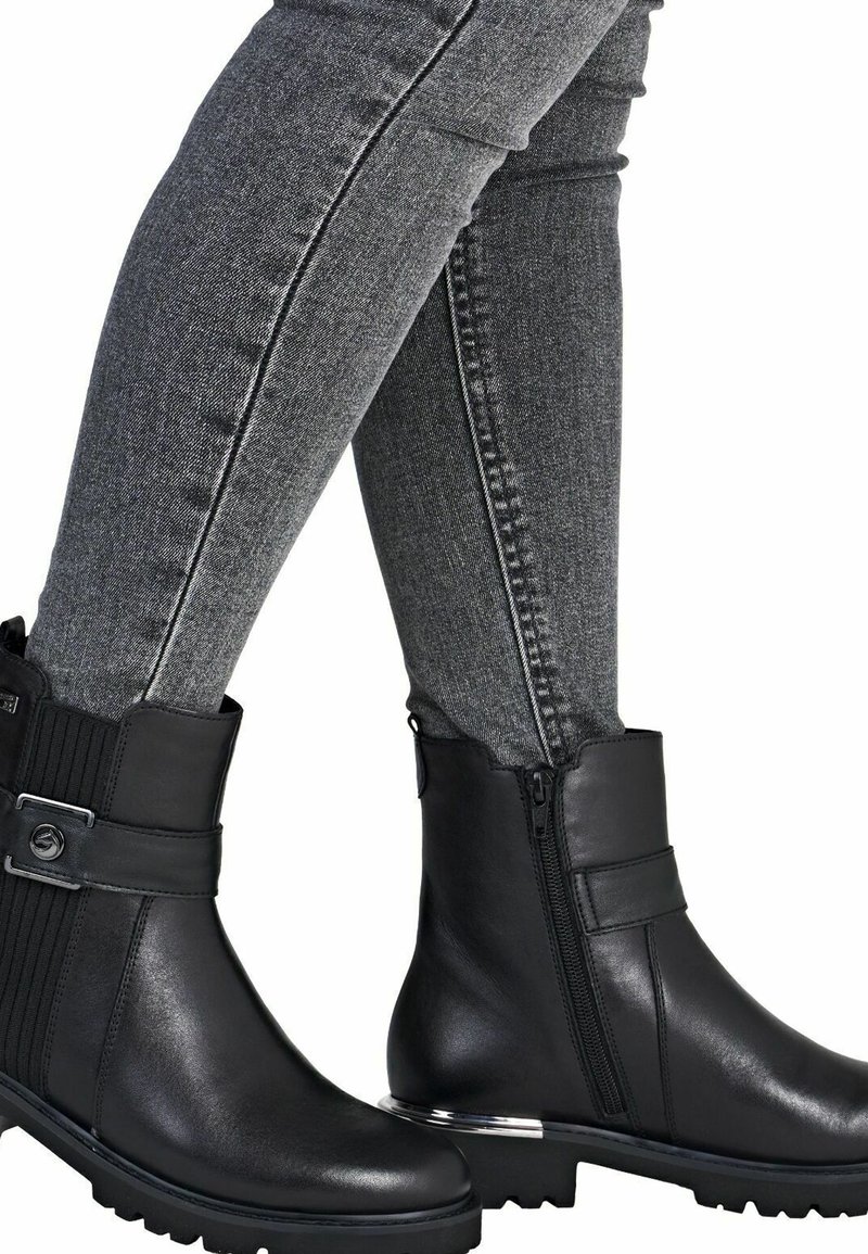 Botines de cuero negro hasta el tobillo con un panel texturizado, cremallera lateral y detalle de hebilla. Cuentan con una suela de goma resistente con agarre.