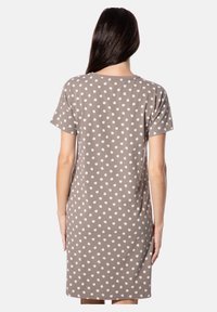 Brauner Tupfenkleid aus weichem Stoff. Kurze Ärmel, lockere Passform und rundlicher Ausschnitt. Die Tupfen sind weiß auf braunem Hintergrund.