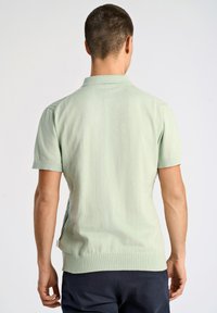 Helles grünes Polohemd mit kurzen Ärmeln und strukturiertem Finish, Seitenschlitzen und geripptem Kragen. Taillierte Passform mit glatter Rückseite.