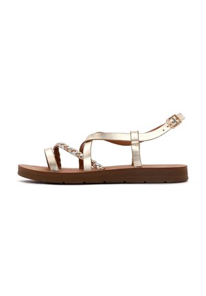 Gold metallic flat sandals feature braided straps, a secure ankle buckle, and a brown textured sole with a slight grip pattern.