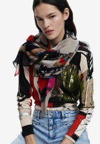 Multicolored scarf featuring abstract patterns in red, black, and blue, wrapped around a model's neck; sheer texture, lightweight fabric.