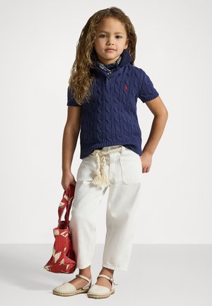 Polo shirt en maille torsadée marine, pantalon blanc ample, espadrilles beiges et un sac rouge à motif géométrique. Les accessoires comprennent un bandana bleu.