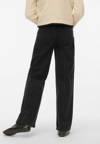 Crne traperice s tankim linijama u slobodnom kroju, srednjeg struka i s dva stražnja džepa. Nošene s džemperom boje kreme.