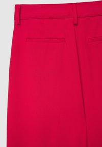 Rote, maßgeschneiderte Hose mit glatter Textur, Gürtelschlaufen und zwei Gesäßtaschen. Der Stoff wirkt strukturiert und figurbetont.