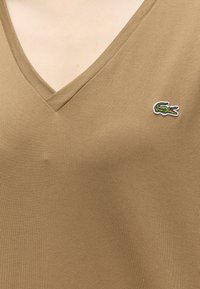 T-shirt beige col en V avec un petit logo crocodile vert brodé sur la poitrine gauche.