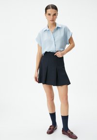 Camisa de botones de manga corta azul claro y falda oscura de rayas con pliegues, combinada con calcetas azul marino hasta la rodilla y mocasines burdeos.